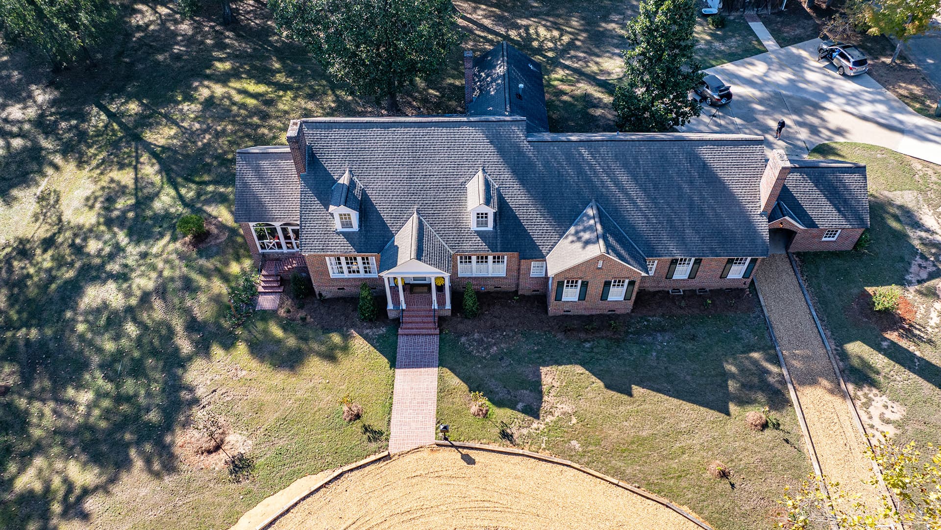 Aerial view of a large brick house with a landscaped yard and a circular driveway.