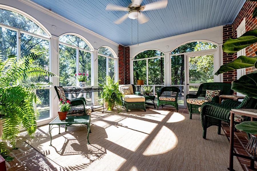 A bright sunroom with large windows, indoor plants, and comfortable seating.