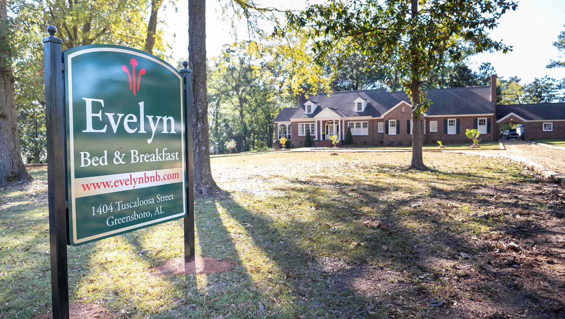 A sign for Evelyn Bed & Breakfast in front of a cozy brick house surrounded by trees.